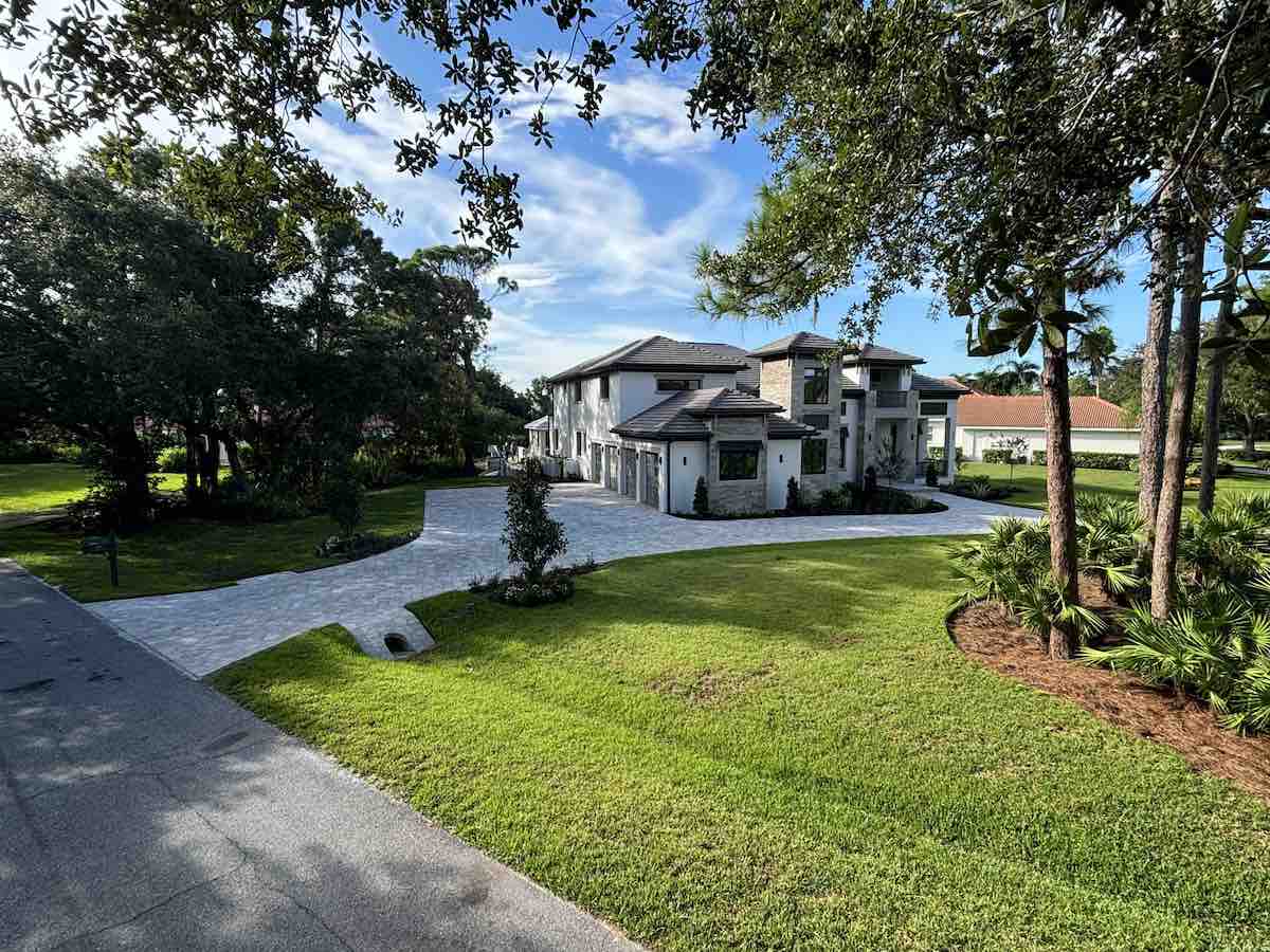 Light-colored paver driveway curving around a landscaped lawn in front of a two-story custom home