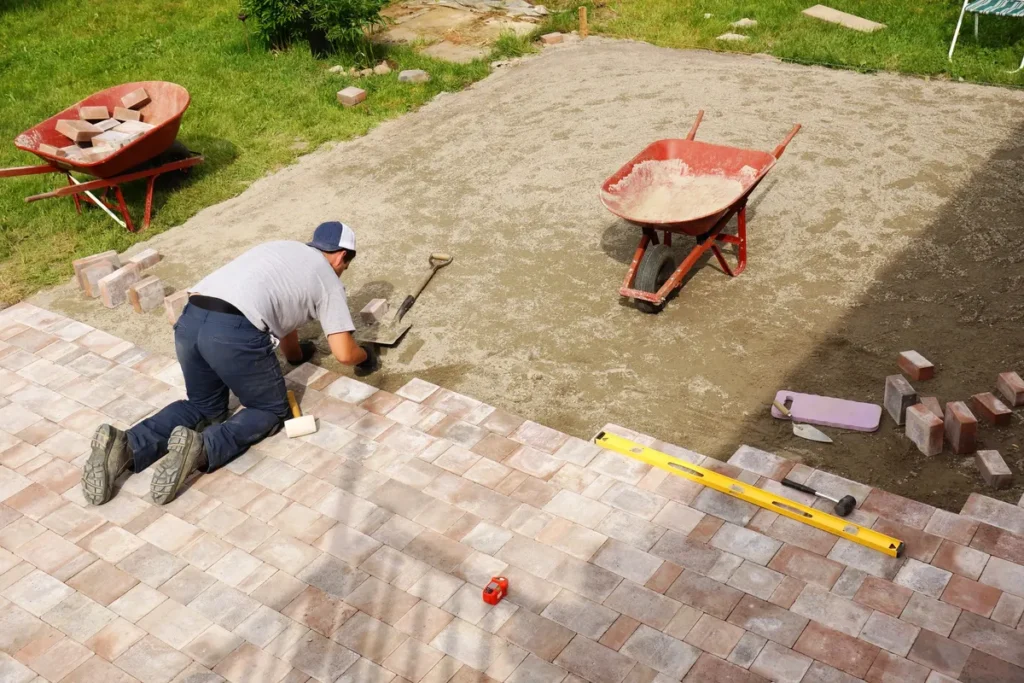 A young man laying paver bricks to create a spacious patio in a backyard, showcasing creative design options.