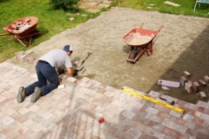 A young man laying paver bricks to create a spacious patio in a backyard, showcasing creative design options.