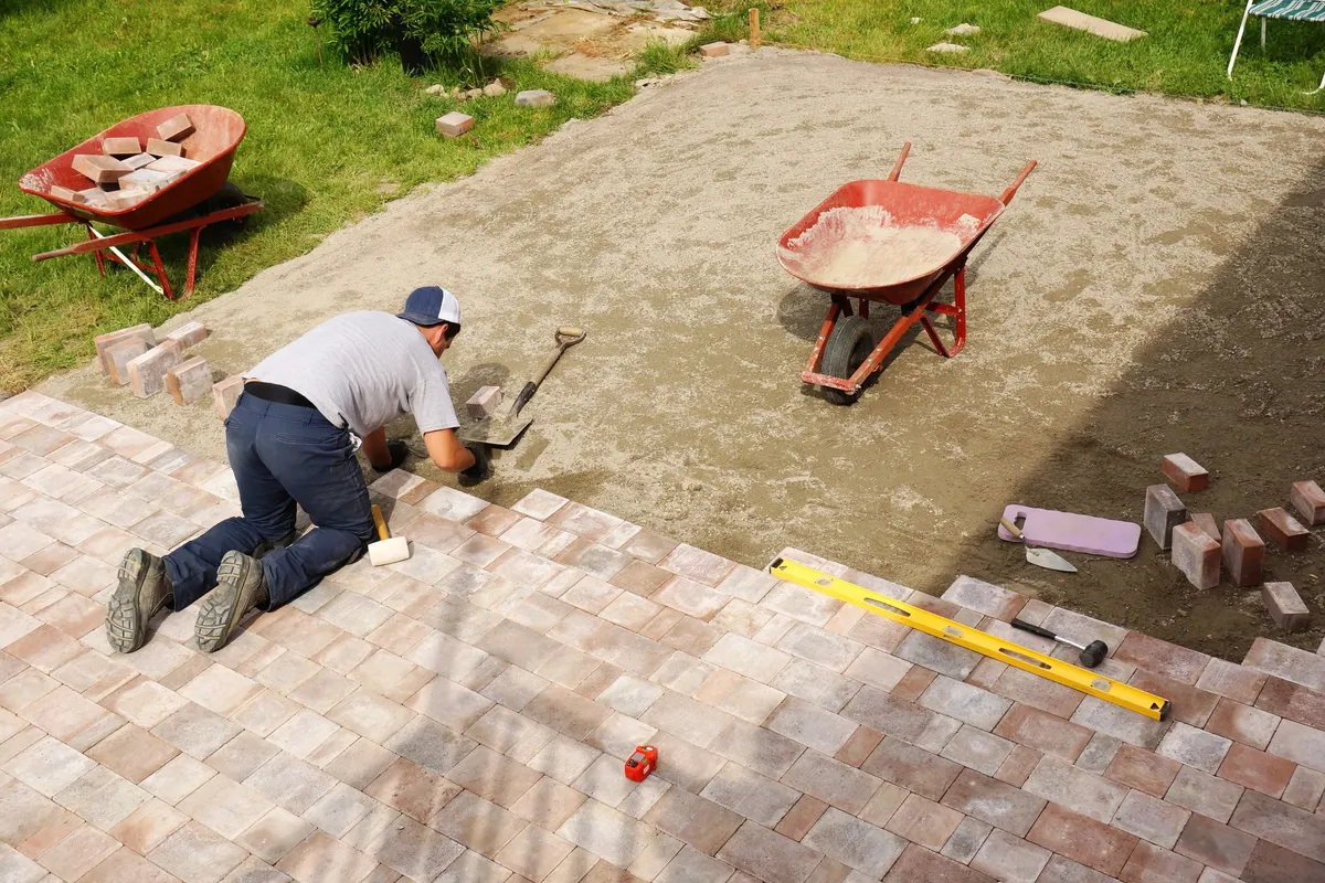 Exploring Creative Paver Designs for Your Venice, FL Outdoor Space 1 A young man laying paver bricks to create a spacious patio in a backyard, showcasing creative design options.