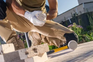 A worker carefully positions a travertine paver while installing a patio, highlighting installation techniques.
